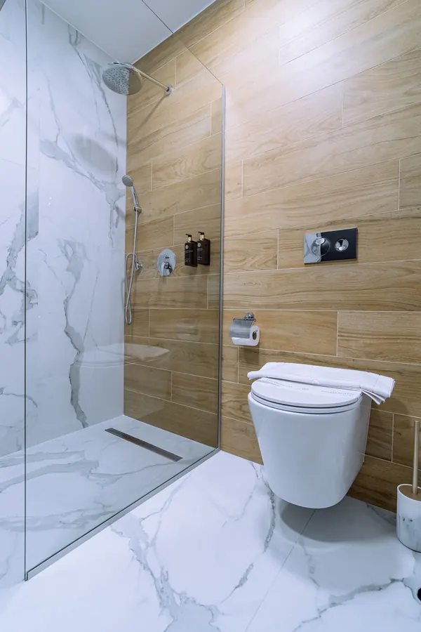Baño con ducha a ras de suelo, mármol blanco y madera