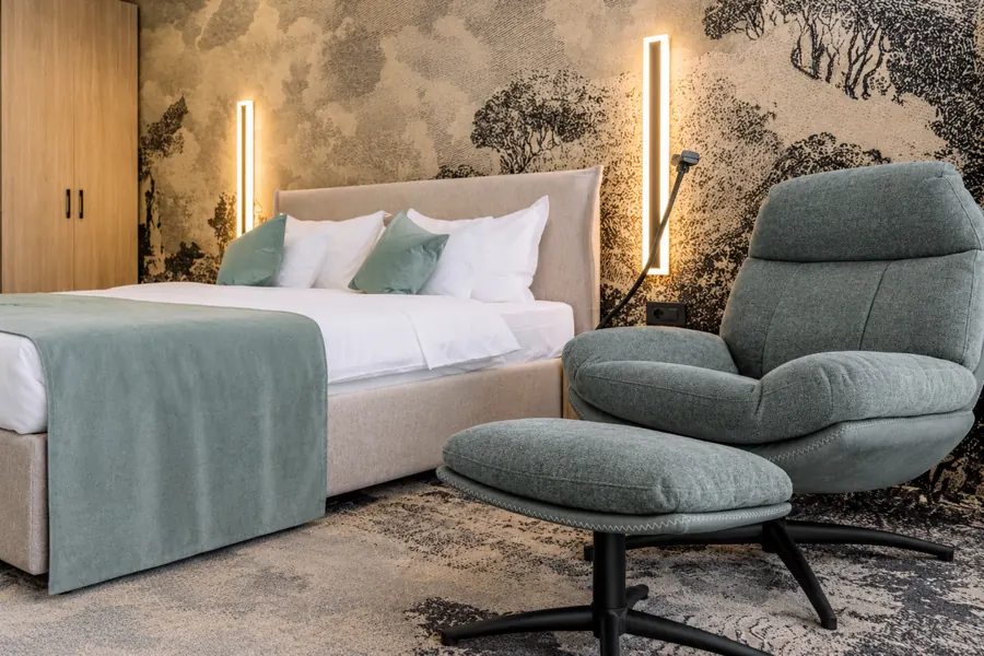 Sillón con reposapiés junto a la cama, ante un paisaje en tonos grises