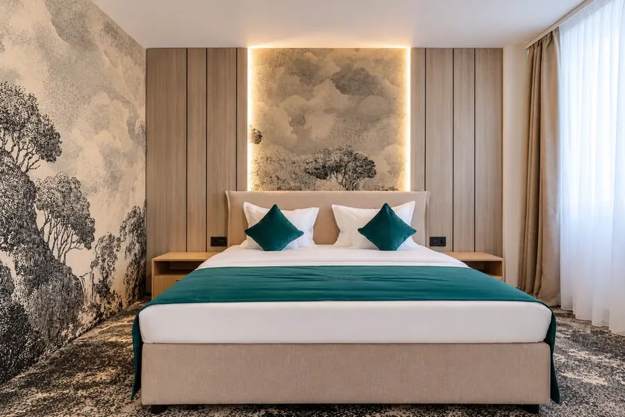 Cama de matrimonio con cojines esmeralda, bajo un paisaje en tonos grises