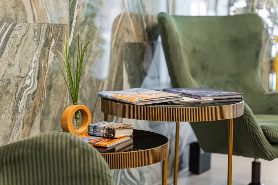 Sillón de terciopelo verde y mesita dorada, sobre un fondo de mármol