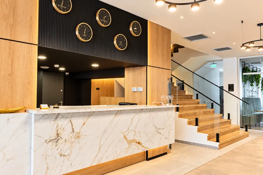 La recepción del hotel, con mostrador de mármol y relojes en la pared