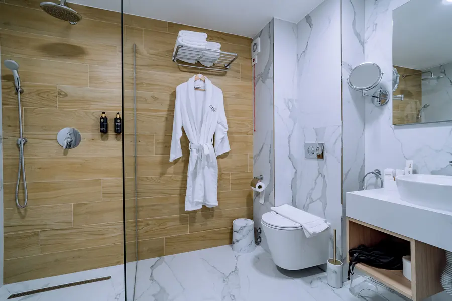 Baño con ducha, albornoz blanco y revestimientos de madera y mármol